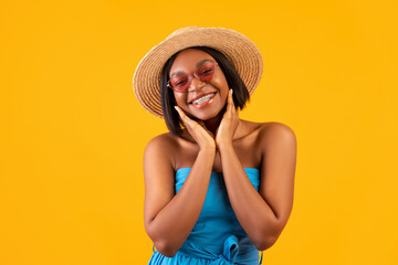 Portrait of gorgeous black woman in casual summer outfit touching her face and smiling at camera on orange background