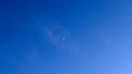 A small moon in a blue sky with a cloud