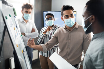 Employee in protective medical mask presenting business strategy on whiteboard