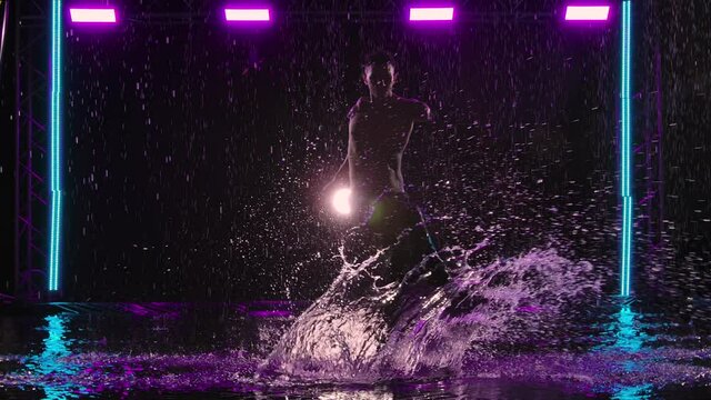 Wet Man Dancing Sensual Modern Ballet On Water Surface In The Rain. Romantic Contemporary Choreography. Silhouette Of Dancer With Naked Torso In Purple Studio Light. Slow Motion.