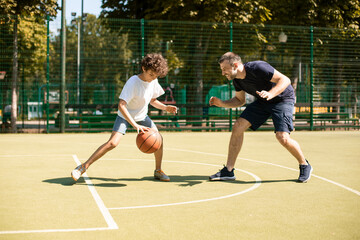 Sportive dad teaching his son how to play basketball outside