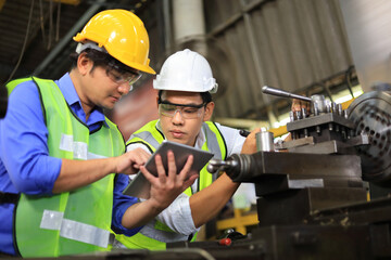 Asian engineering manager and mechanic worker in safety hard hat and reflective cloth using lathe...