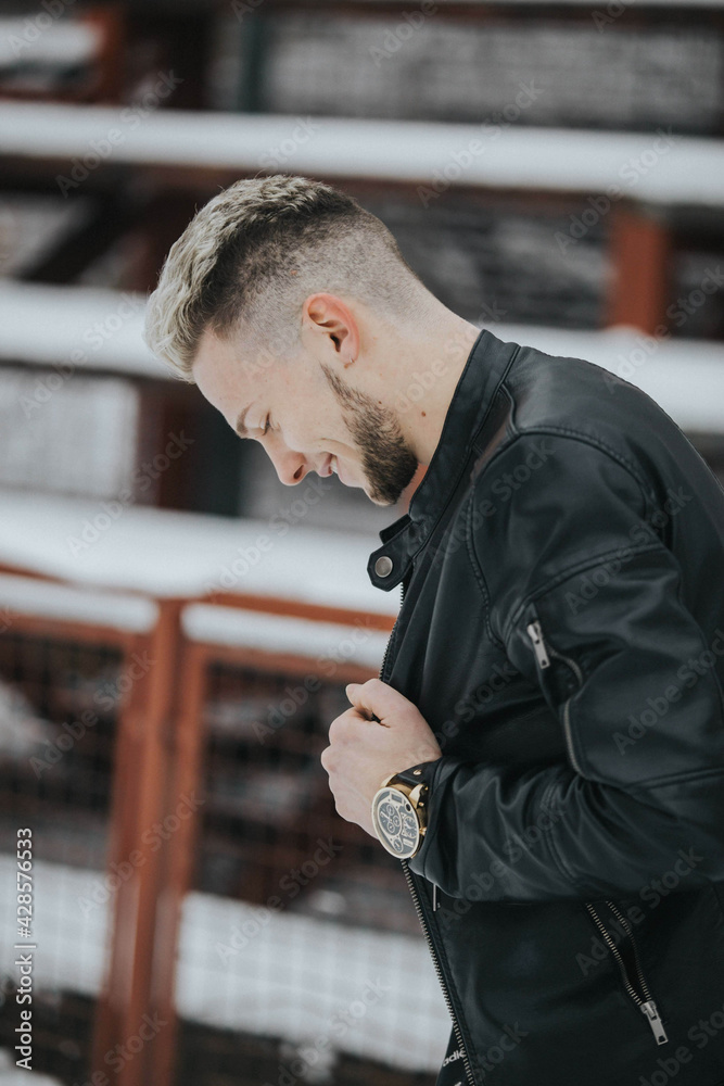 Wall mural Shallow focus shot of a handsome smiling man in a black winter street style outfit in a snowy park