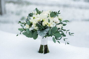 Beautiful bridal bouquet of white flowers and greenery, decorated with long silk ribbon lies on white background.