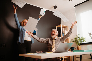 A happy photo of an elderly couple who heard good news and happily throws papers in the air.