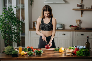 Fit young woman cooking fresh salad at home standing in kitchen adding exotic spices to mixture. Healthy eating concept.