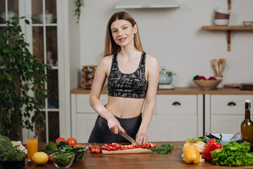 Fit young woman adding spices to salad mixture, cooking fresh meal at home in kitchen. Healthy eating concept.