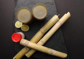 Sugarcane juice in glass with piece of sugarcane, lemon and black salt 