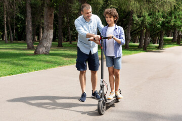 Boy learning to ride e-scooter with his adult dad