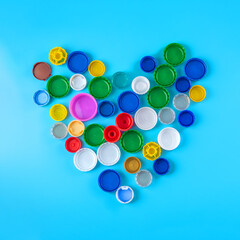 Heart made of colorful plastic bottle caps on a blue background, collecting plastic for recycling and reuse.