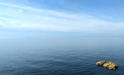 Marine panorama a blue expanse where the sea meets the sky with a single orange rock in the foreground