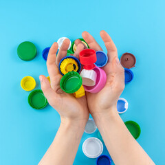 Colorful plastic bottle caps in women's hands on a blue background, collecting plastic for recycling and reuse.