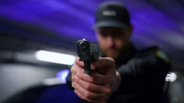 Policeman aiming gun during operation. Male cop with firearm posing at camera