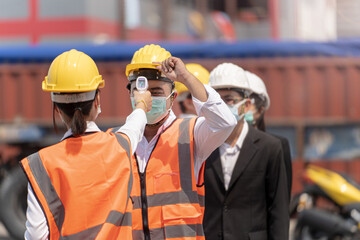 Factory woman worker in a face medical mask and safety dress used measures temperature at worker...