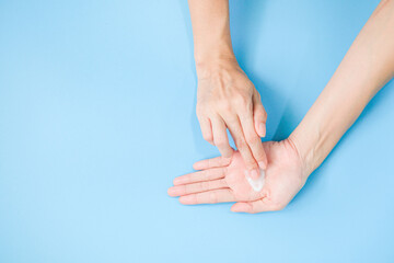 Woman applying moisturizing hand cream on hand with blue background, Health care concept.