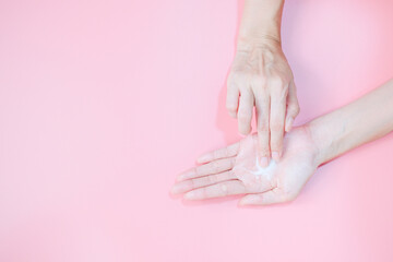 Woman applying moisturizing hand cream on hand with pink background, Health care concept.