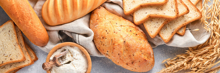 Various crispy breads and buns, wheat flour and ears on light gray concrete background table. Top view flat lay. Banner.