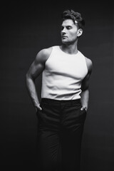 Monochrome portrait of a handsome young man with stylish haircut in a white undershirt and black pants. Studio shot.