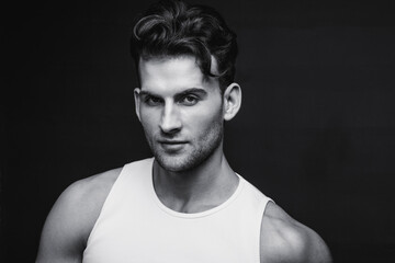 Monochrome portrait of a handsome young man with stylish haircut in a white undershirt. Studio shot.