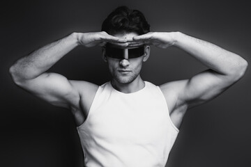 Monochrome portrait of a handsome young man with stylish haircut in a white undershirt, black pants and glasses. Studio shot.