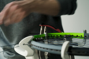 Close-up of tennis racket on electronic stringing machine. Process of replacement synthetic gut string before game. Hands of stringer in motion.