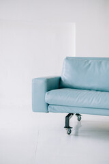 Blue leather modern sofa in bright living room with white walls, minimalistic interior.