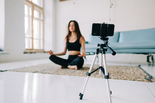 Beautiful brunette fitness woman meditate in front camera on tripod, doing yoga at home. Staying fit and healthy