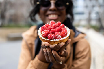 African American black woman is sitting outside enjoying a delicious pastry while smiling and being...