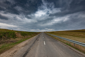 Naklejka premium Asphalt road leading to the top of the hill, dramatic gathering stormclouds at spring.