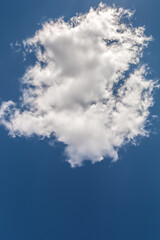 A fluffy cloud against a dark blue sky. Vertical natural background.