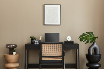 Stylish composition of home office interior with black wooden desk, chair, tropical flower in vase, laptop, mock up poster frame, cup of coffee, clock and elegant office accessories. Template.