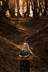 Girl playing the harp at sunset in the forest