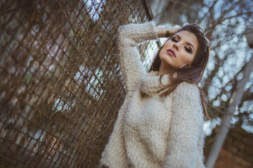 Low angle shot of a confident brunette woman leaning against afence wearing a turtleneck sweater