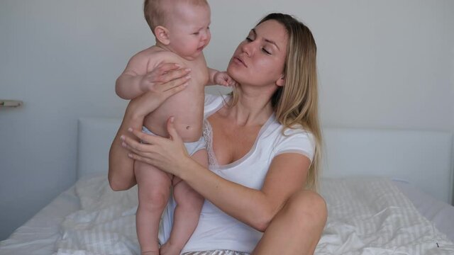 A young mother rocks the baby in her arms. The baby cries and does not want to sleep.