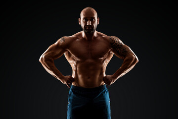 Fototapeta na wymiar Tattooed male bodybuilder posing over black background. Fitness workout concept, muscle groups, watch your body.