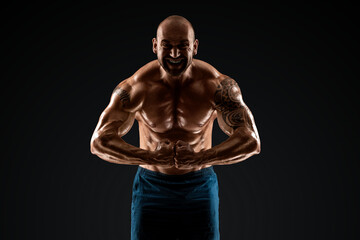 Fototapeta na wymiar Tattooed male bodybuilder posing over black background. Fitness workout concept, muscle groups, watch your body.