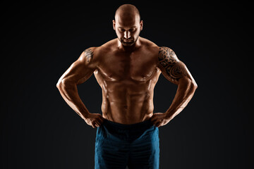 Obraz na płótnie Canvas Tattooed male bodybuilder posing over black background. Fitness workout concept, muscle groups, watch your body.