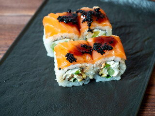 side view of juicy delicious rolls decorated with caviar. Japanese cuisine, black plate, close up