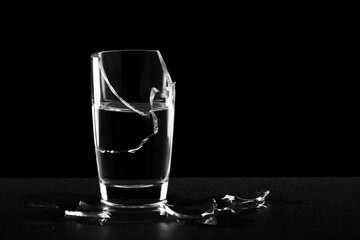 against a dark background, a broken glass of water, the shards lie next to the glass