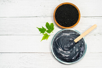 Homemade face mask and scrub with activated charcoal powder and yogurt on white wooden background