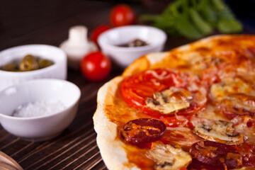 Homemade pizza with pepperoni sausage, bacon decorated spinach and ingredients on the background.