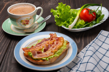 sandwich with fried bacon on a lettuce leaf and a cup of coffee
