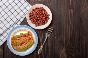 breakfast with a sandwich with fried bacon, beans and lettuce top view