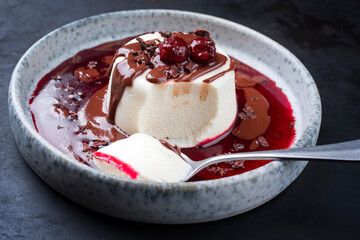 Modern Style traditioneller Blancmange Mandel Pudding mit Kirschen, Schokoladen Creme und Sauerkirsch Kompott Coulis serviert als close-up auf einem Nordic Design Teller