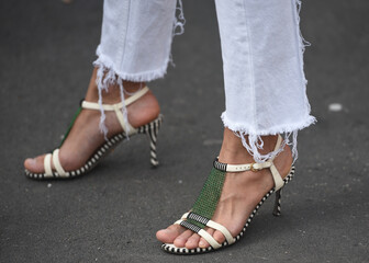 Detail of a fashionable outfit –woman wearing white pants and white sandals with metal details