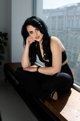 Pretty girl sitting on the window. Sunny day on the city. Dark hair girl on the city.
