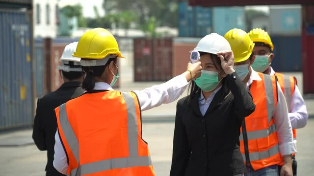 manager wear face mask scanning body temperature and using hand sanitizer alcohol gel to worker before entering working over Containers box at logistic Cargo during Coronavirus or Covid 19 pandemic