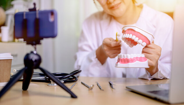 Asian dentist woman working online at home. Recording blog video for tutorial instructional brushing teeth clean. Dentistry and teeth health care.
