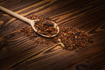 Chocolate granola cereal with nuts in a wooden spoon.