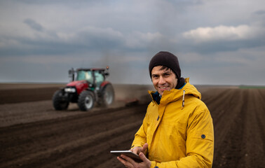 Farmer with tablet in front of tractor in field
